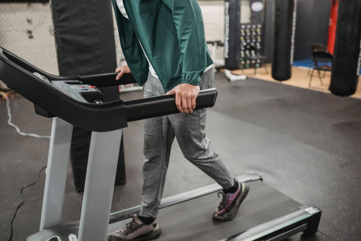 An older man walking on a treadmill at home beside a window